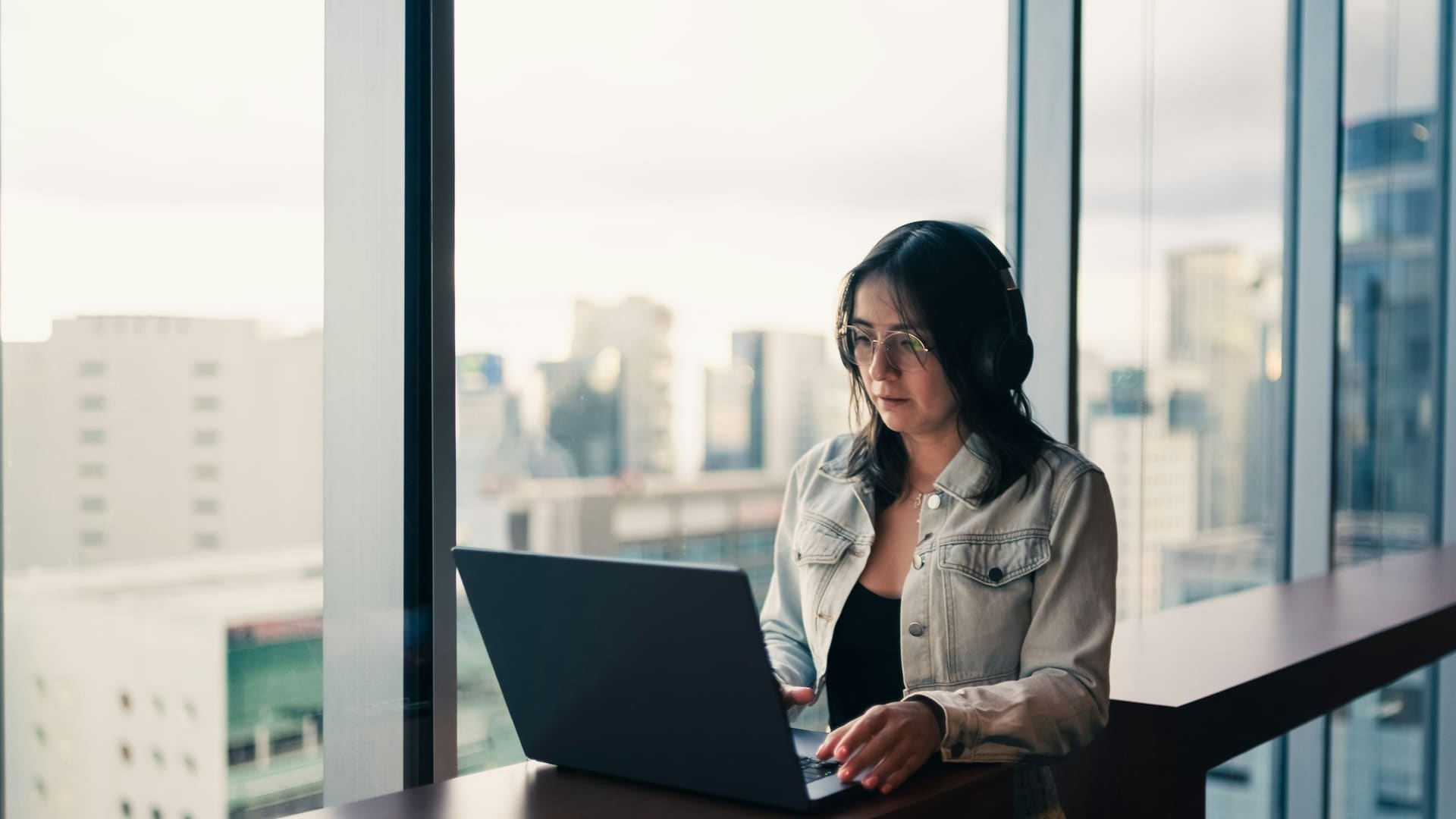 Woman wearing headphones working on a laptop by window