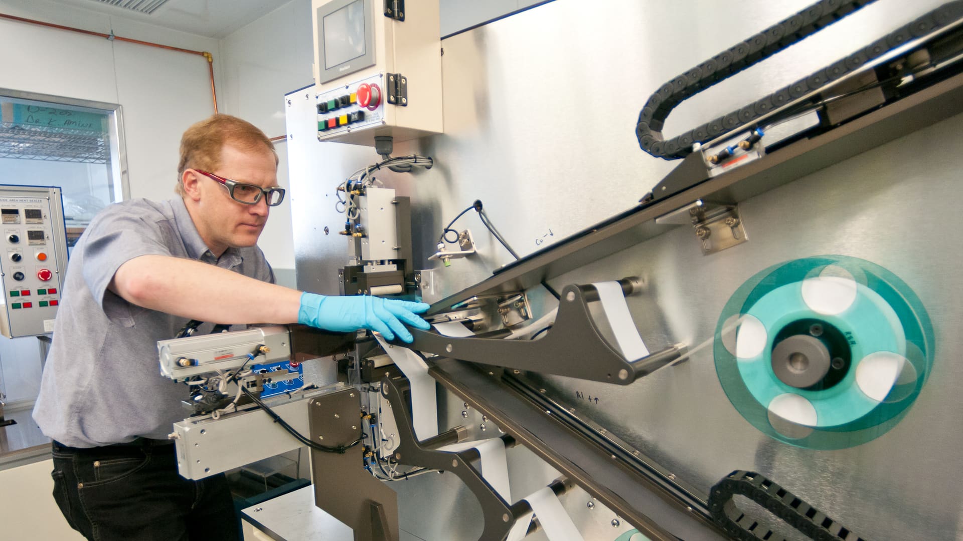 Argonne lab worker aligns battery electrode sheets on a winder machine that rolls lithium-ion cell layers together