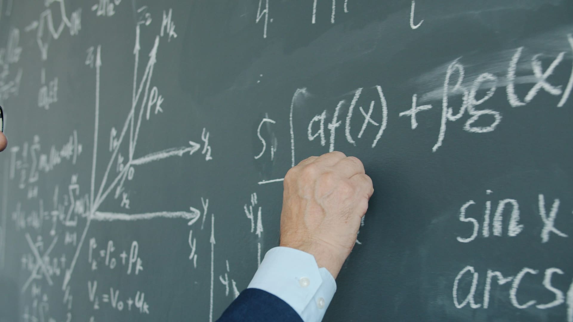 Close-up of a man's hand holding chalk and underlining a mathematical formula on a chalkboard