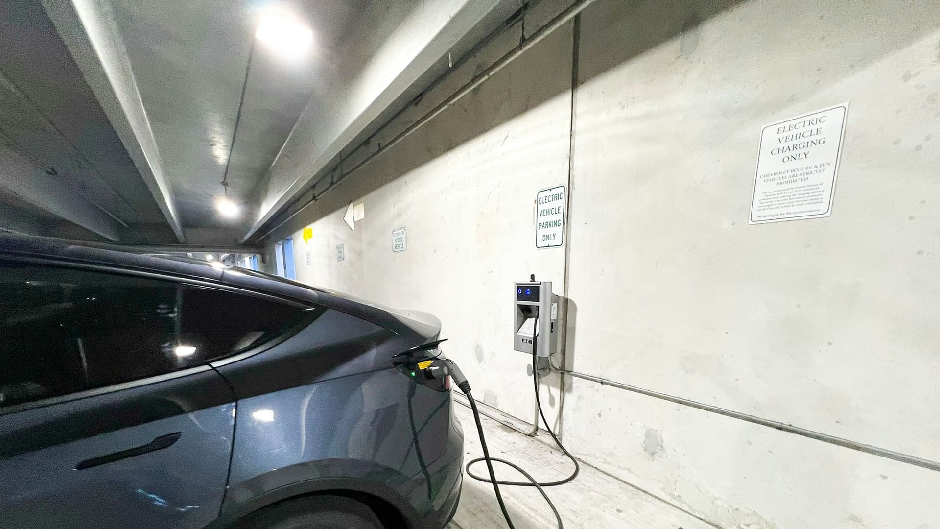 A Tesla plugged into a charger in a parking garage.