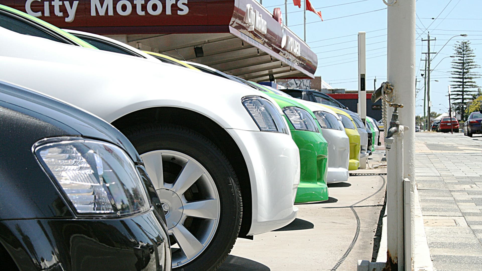 A row of colorful new cars parked at a car dealership lot under a bright blue sky