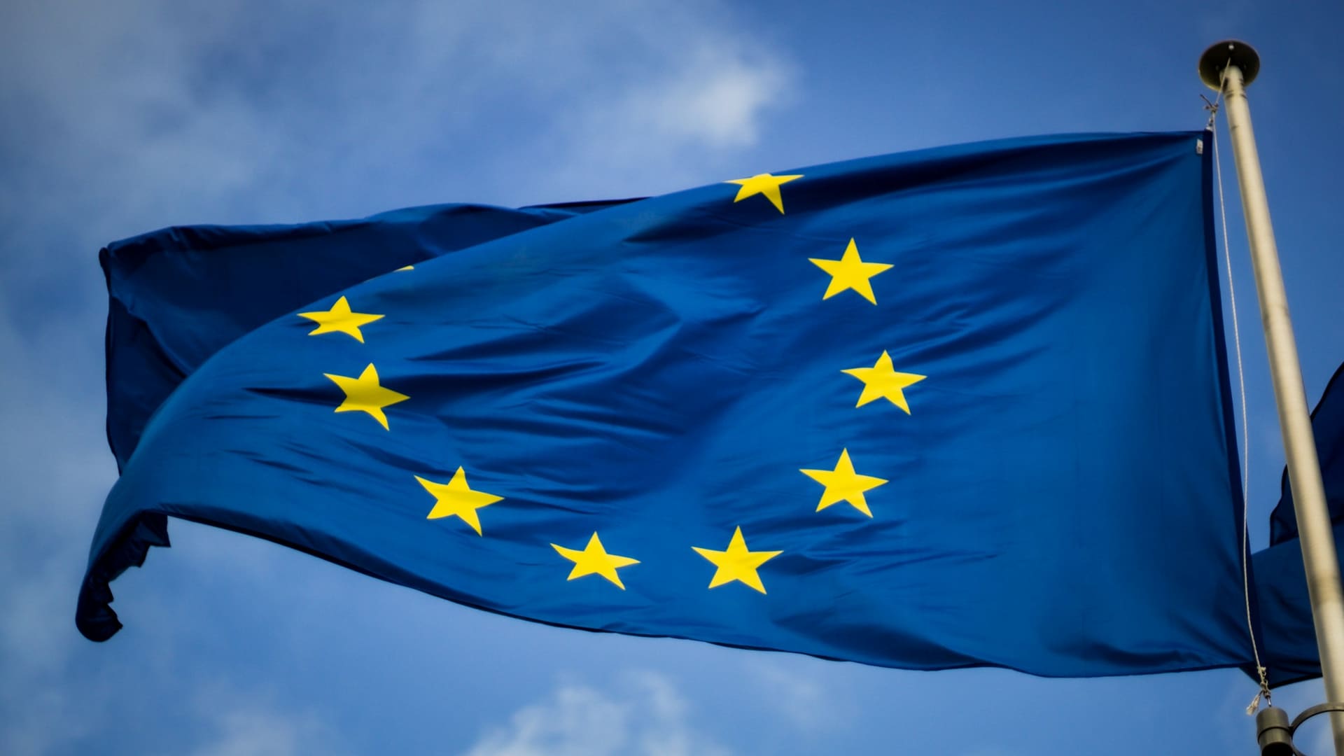 EU flag with blue and yellow stars in front of European Parliament, Brussels