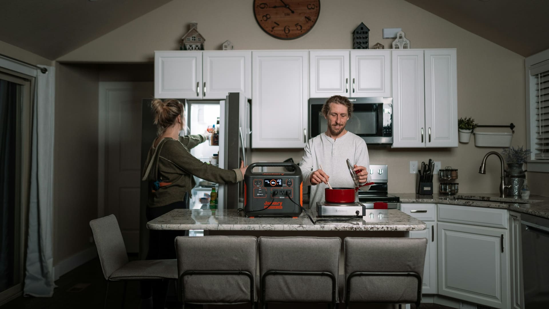 Two people standing in a kitchen with a portable power station supplying power to household devices