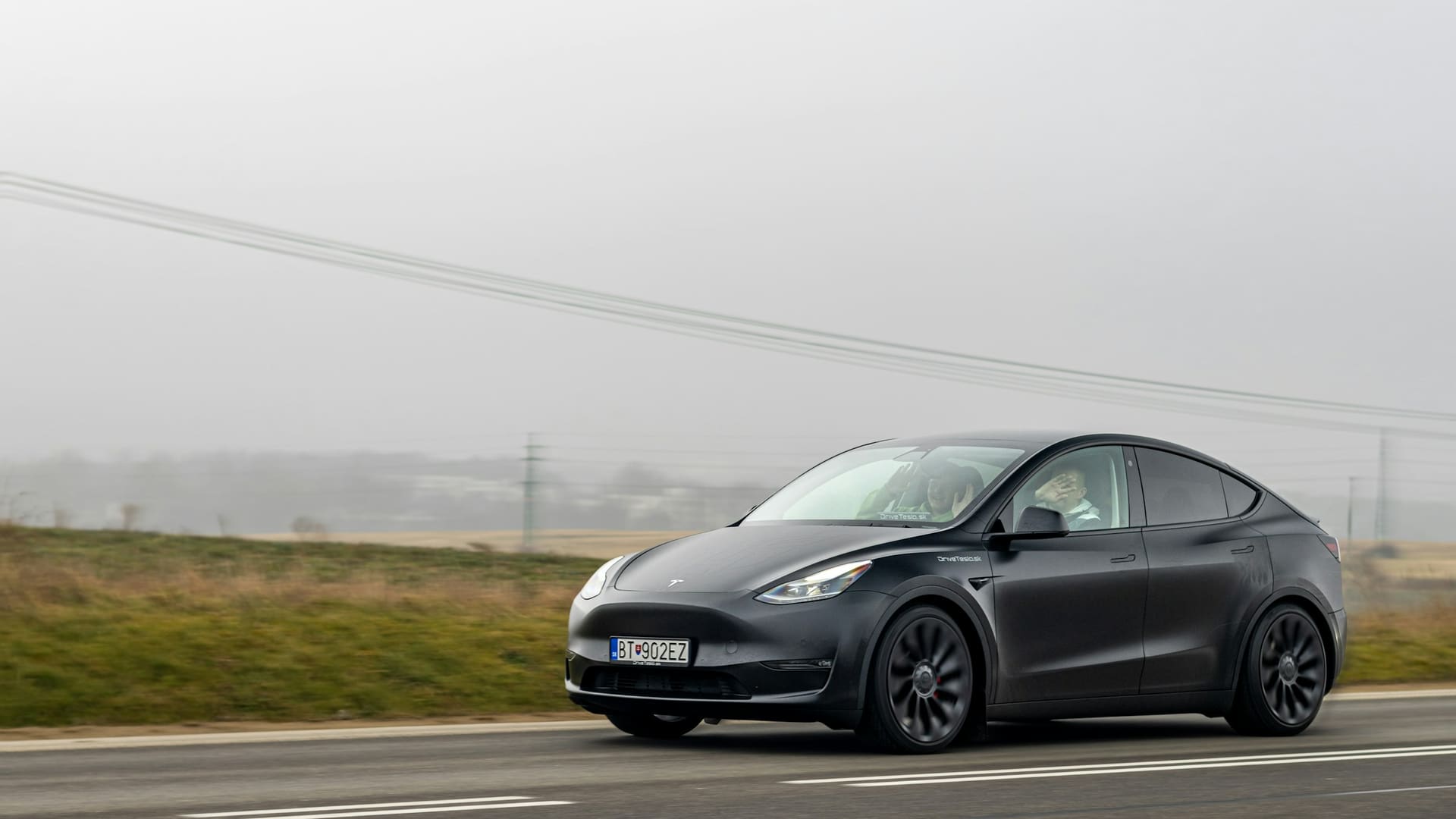 Tesla Model Y driving on country road with people waving