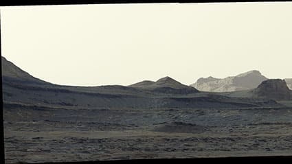 Curiosity Mastcam sunrise panorama of Mars: blue-tinted foreground, sunlit wind-carved yardang cliffs on the horizon